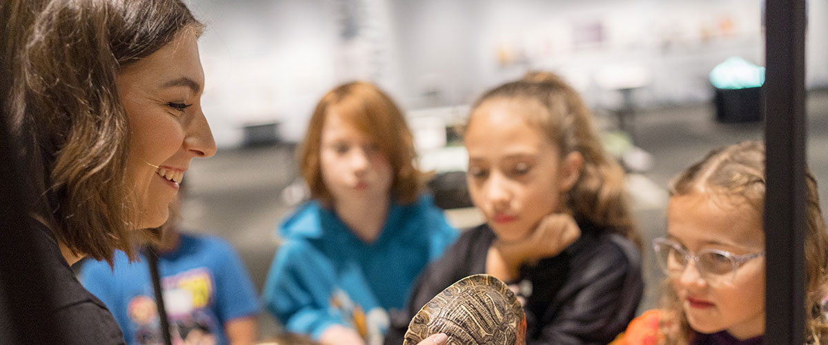 A facilitator shows a turtle shell to three children.