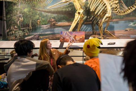 An Educator holds up a storybook as they read out loud to a group of kids in one of the Royal Alberta Museum Galleries.