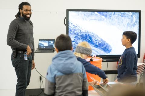 A smiling Museum staff member talks to a group of kids.