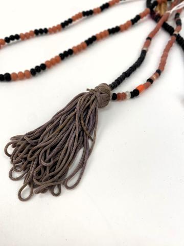 A close-up view of a tassle on the end of an orange and black beaded necklace. 