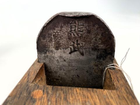 A close up of a metal blade on a wooden plane tool. Japanese characters are embedded in the metal blade. 