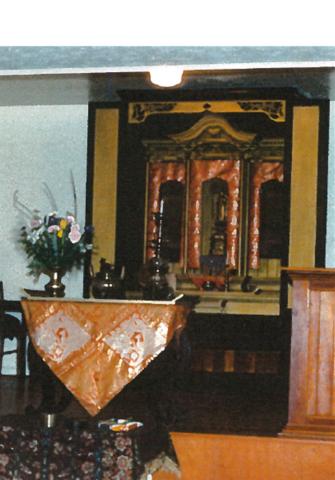 A photo of a Buddhist shrine in Picture Butte, Alberta. The shrine is a dark wood, with orange and yellow details.