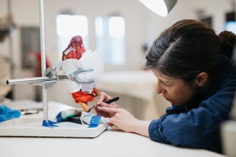 A close-up of a person peering closely and doing conservation work on an object. The object is obscured, so we are unable to see exactly what it is.