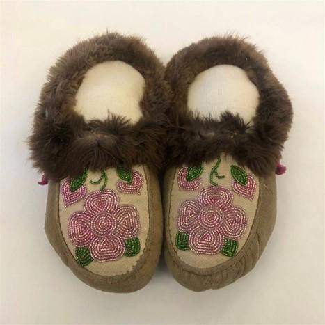 Two light brown moccasins. The moccasins have pink flowers beaded on the top and dark brown fur around the ankle.